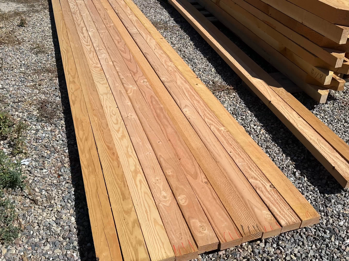 Douglas fir slats and beams for a 12×16 pergola, cut to length and marked, laid out on gravel before staining