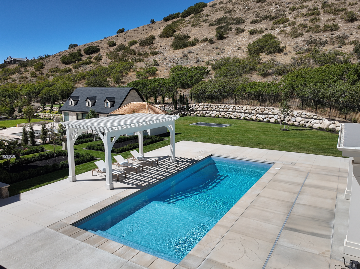 Aerial view of the Pinto White pergola beside the pool in Alpine, Utah, with the pool house and hillside behind
