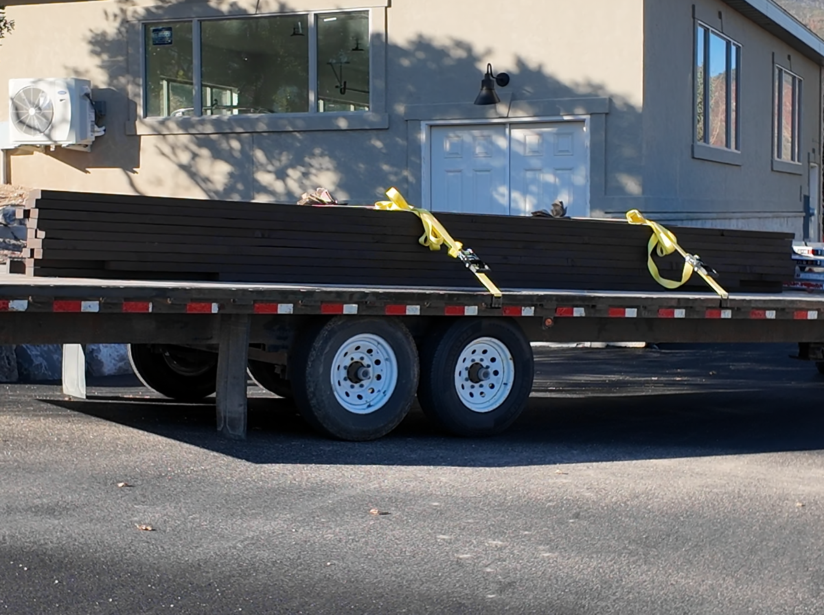 Cordovan Brown timbers for an 18×18 pergola strapped down on a flatbed trailer at the job in Elk Ridge, Utah, on install morning